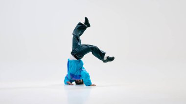 Klasik giyinmiş dansçı amuda kalkarken, kolları tamamen beyaz arka plana uzanmış. Vücut yerçekimiyle aynı hizada. Denge kavramı, güç, kontrol, şehir dansı, hareket.