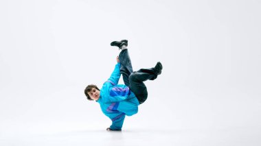 Klasik giyinmiş dansçı, hareket halinde, beyaz stüdyo arka planına karşı yer çekimine meydan okuyan bir hareketle askıya alınmış. Akrobatik kavramı, sanatsal hareket, çağdaş dans, şehir tarzı..