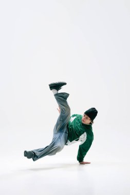 Şehir dansçısı, klasik giyinmiş, akrobatik dönüş yapan, beyaz arka plana karşı hassasiyetle yerçekimine meydan okuyan. Dans ve müzik kavramı, sanat, kontrol, ifade, modern sokak kültürü.