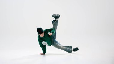 Şehir dansçısı, klasik giyinmiş, akrobatik dönüş yapan, beyaz arka plana karşı hassasiyetle yerçekimine meydan okuyan. Dans ve müzik kavramı, sanat, kontrol, ifade, modern sokak kültürü.