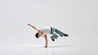 Breakdansçı, kot pantolon ve beyaz tişört, vücudunu havadan hareketsiz bir pozisyona sokma ve beyaz arka plana yoğun odaklanma. Dans, retro, özgürlük, kontrol, performans kavramı.