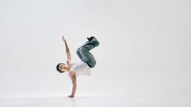 Sokak göstericisi, beyaz arka plana karşı güç ve teknik hassasiyeti somutlaştırarak, geriye doğru hareket ediyor. Dans ve müzik kavramı, sokak tarzı, şehir kültürü, kontrol, denge, hareket.