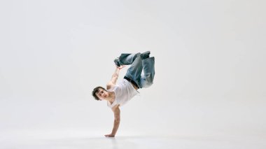 Modern, yetenekli sokak dansçısı, günlük kıyafetler giymiş, ters takla atmış, beyaz arka planda hareket halindeki vücut kontrolünü gösteriyor. Spor, sanat, serbest stil, çeviklik, müzik, sanatsal ifade kavramı.