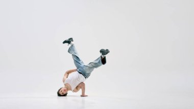Yetenekli break dansçıların dinamik fotoğrafı bir elinde baş aşağı, bacaklarında beyaz arka planda bükülmüş. Spor, sanat, müzik, güç, aktif yaşam tarzı, ritim, hareket kavramı
