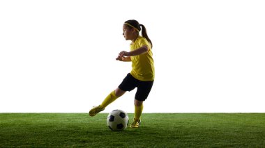 Çocuğun dinamik görüntüsü, sarı formalı kız ve çimenli yüzeyde hareket eden siyah gömlekli kız, beyaz stüdyo arka planına top sürüyor. Spor, çocukluk, hareket, rekabet, etkinlik kavramı