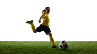 Spor üniformalı kendine güvenen kız topu özenle kontrol ediyor çimenli zeminde beyaz stüdyo arka planıyla futbol oynuyor. Spor, çocukluk, hareket, rekabet, etkinlik kavramı