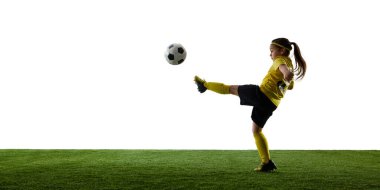 Kızın dinamik görüntüsü, çimenli sahada hareket eden bir futbolcu, beyaz arka planda bir bacağı açık topa vuruyor. Spor, çocukluk, hareket, rekabet, etkinlik kavramı