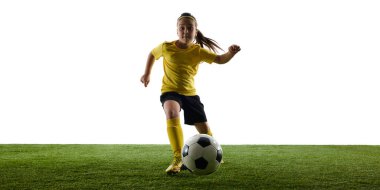 Odaklanmış kızın dinamik görüntüsü, hareket halindeki futbolcu, antrenman yapan, çimen yüzeyinde beyaz stüdyo arka planına karşı top süren top. Spor, çocukluk, hareket, rekabet, etkinlik kavramı
