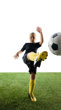 Siyah üniformalı, sarı çoraplı, topa vuran, beyaz stüdyo arka planında çimenli yüzey eğitimi alan odaklanmış bir kızın ön görüntüsü. Spor kavramı, çocukluk, rekabet, etkinlik