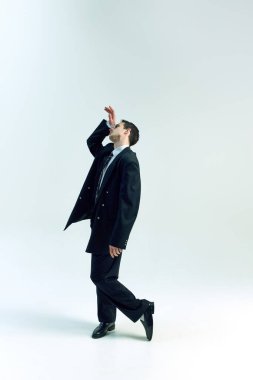 Beyaz stüdyo arka planına nazikçe yaslanmış, el kaldırarak etkileyici bir iş adamı pozu veren uzun bir fotoğraf. İş kavramı, psikoloji, içgözlem, kurumsal stres.