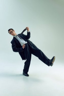 İş adamı kravatını şakacı bir şekilde çekiyor, geriye yaslanıyor, tek bacağıyla beyaz stüdyo arka planında dengede duruyor. İş, psikoloji, stres, tükenme, aşırı çalışma, iş-yaşam dengesi kavramı.