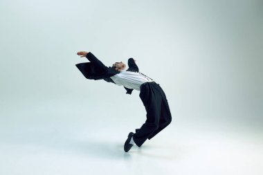 Genç işadamı, beyaz stüdyo arka planına karşı ceketiyle geriye doğru eğiliyor. İş, psikoloji, özgürlük, aşırı çalışma, iş hayatı dengesi kavramı.