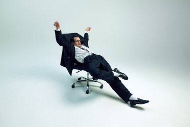 Genç ve bitkin bir iş adamı gevşek duruşu olan tekerlekli sandalyeye yaslanıyor ve beyaz stüdyo arka planına yaslanıyor. İş kavramı, psikoloji, aşırı çalışma, iş hayatı dengesi.