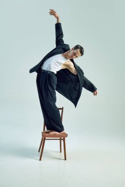 Tahta sandalyede dengede duran yalın ayaklı bir adam dramatik bir iş duruşu içinde beyaz zemine karşı risk ve istikrar arasındaki gerilimi ifade ediyor. İş kavramı, psikoloji, aşırı çalışma, iş hayatı dengesi.