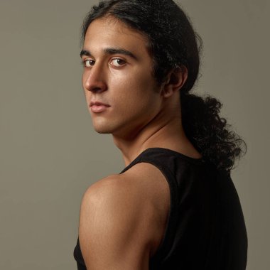 Kendine güvenen, derin bakışlı, yüzü tanımlanmış, omuzlarının üstünden bakan, koyu kıvırcık saçlı, kendine güvenen genç bir adam. Doğal güzellik kavramı, cilt bakımı, kozmetik, erkek sağlığı.