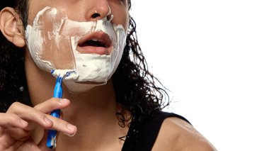 Traş olurken çekilmiş yakın plan bir resim. Beyaz stüdyo arka planına karşı yoğun köpükler arasında jilet gibi süzülüyor. Erkek güzelliği, bakımı, traşı, kendine bakımı, kozmetik ürünleri, reklamı.