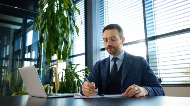 Modern ofiste kurumsal büyüme planlarını düzenlerken kendini not almaya adamış bir yönetici. İş planlama, üretkenlik, yenilik, liderlik kavramı.