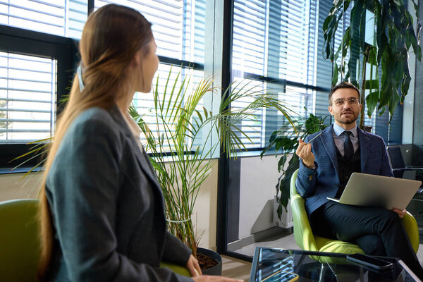 Молодой предприниматель внимательно слушает делового партнера, работая над ноутбуком в стильном рабочем пространстве. Концепция предпринимательства, современный бизнес, цифровые преобразования, адаптивность.