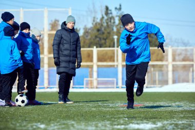 Bina Koordinasyonu. Genç futbolcu dışarıda karlı stadyumda top sürme hızı ve çeviklik eğitimi alıyor. Motivasyon ve ilerleme. Hazırlık kavramı, disiplin, çocukluk hırsı.