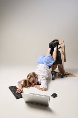 Yorgun genç bir kadın alışılmadık bir ofis pozisyonunda, klavyeye yazı yazıyor, sonu gelmeyen, gri şirket rutinini yansıtıyor. İşçilik kavramı, aşırı çalışma, kariyer baskısı.