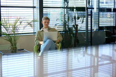 Günümüz ofis alanında dizüstü bilgisayarda çalışan genç profesyonel jaluzilerden güneş ışığı geçiyor. İş kavramı, üretkenlik, teknoloji, çalışma alanı.