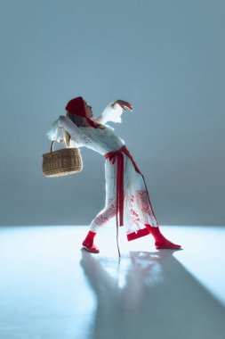 Beyaz-kırmızı kıyafetli etkileyici bir genç kadın, sepetle geriye doğru eğiliyor, hareketi hikaye anlatımı olarak somutlaştırıyor, dönüşümü ve iç çatışmayı sembolize ediyor. Moda, dans, sanat kavramı.