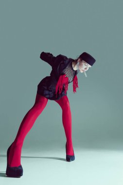 Siyah giysili genç bir kadın, kırmızı tayt ve delici bakışlarla öne eğilen ağlı bir şapka. Moda hikaye anlatımı kavramı hareket, gerçeküstü mistisizm, trendler.