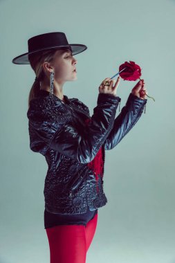 Geniş kenarlı şapkalı mistik kadın yumuşak arka planda fırçayla kırmızı gül boyuyor. Sanat, moda, güzellik, sembolizm, sürrealist moda, psikoloji.