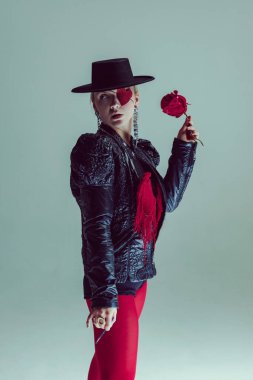 Keskin bakışlı hayalperest kadın solmuş gül tutuyor, tutku ve kontrol arasındaki gerilimi somutlaştırıyor. Aşk kavramı performans, geçici duygular, şiirsel sürrealizm, moda, güç.