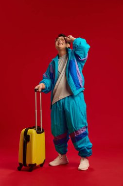 Genç bir adamın tam boy fotoğrafı, spor giyinmiş, çantasıyla poz veriyor ve yukarı bakıyor, uçağın kırmızı arka planına bakıyor. İnsan duyguları kavramı, seyahat, rezervasyon hizmetleri. Ad