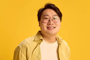 Neşeli genç adamın yakın portresi, güvenle kameraya bakıyor, güneşli sarı arka plana karşı pozitif paylaşıyor. İnsani duygular, görünüş, mutluluk kavramı. Ad