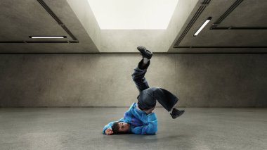 Breakdansçı, eski mavi ceketiyle, kentsel gri beton odada yumuşak ışıkla kafa üstü dönüyor. Sokak enerjisi kavramı, beat, gençlik, dans, hızlı hareket, vahşi ruh, şehir hayatı, saf ifade.