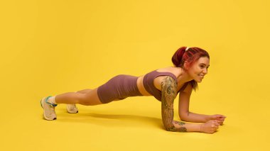 Odaklanmış bir kadın, sarı stüdyo arka planına karşı mükemmel bir formda ön kol kalası tutuyor. Çekirdek kuvveti ve dayanıklılığı var. Vücut kontrolü, eğitim, fitness dengesi, sağlıklı yaşam tarzı kavramı.