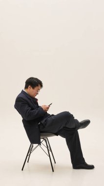 Sandalyede oturan, akıllı telefon kullanan, beyaz arka planda gezinen ya da sohbet eden Asyalı genç bir adamın yan görüntüsü. İnsan duyguları, iş, girişimcilik, hukuk kavramı.