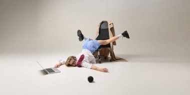 Ofis çalışanı, dizüstü bilgisayarla çalışırken sandalyede baş aşağı dengede duruyor, iş-yaşam dengesizliğini yansıtıyor. Kurumsal tükenme kavramı, akıl sağlığı, iş sorunları. Ad