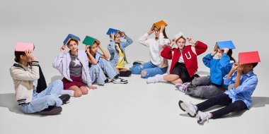 Bir grup öğrenci kafaları üzerinde dengeli kitaplarla çember halinde oturur, yukarı bakar, çalışmak için eğlenceli ve yaratıcı bir yaklaşımı temsil eder. Bilgi günü, fantezi, eğitim, arkadaşlık, edebiyat konsepti.