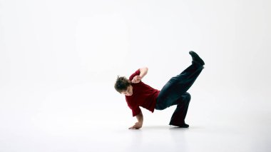 Breakdansçı, sokak kıyafetleri giymiş, bir elinde beyaz arka planda alçaktan dönüyor, hareket sorunsuz. Ritim kavramı, dans enerjisi, güç, çağdaş şehir hareketi, serbest stil.