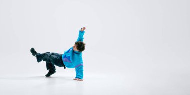 Breakdansçı şık kıyafetler giyer, amuda kalkarak donar, bacaklar yukarı tekme atar, beyaz arka plana yaslanır. Break dans, spor, yaratıcı ifade, enerji, hareket, tutku kavramı.