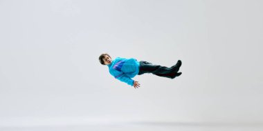Klasik giyinmiş break dansçı, beyaz stüdyo arka planına karşı orta hareketli sıçrayış. Zamanda donmuş bir an. Aşırı hareket kavramı, fiziksel sanatçılık, müzik, enerji, tutku, performans.