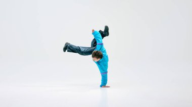 Genç break dansçı, klasik giyinmiş, elinde beyaz arka planda hareket eden bacaklarla dengede duruyor. Spor, dans, müzik, yaratıcılık, aktif yaşam tarzı, kentsel kültür kavramı.