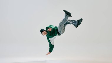 Genç hip-hop dansçısı, retro ceket ve pantolon giymiş, vücut yer çekimine meydan okurken dinamik dondurucu performans sergiliyor temiz beyaz arka plana karşı. Spor, hareket, aktif yaşam tarzı, dans, enerji kavramı.