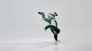 Şehir sanatçısı, retro giyimli, yerçekimine meydan okuyan pozlar veren, beyaz stüdyo arkaplanına karşı hareketli bir vücut. Sanat, müzik, spor, akıcılık, breakdance kültürü, ritim kavramı.