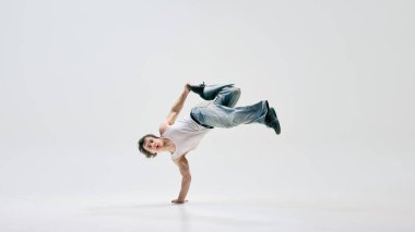 Becerikli bir break dansçı, gelişigüzel giyinmiş, havadan güçlü bir hareket sergiliyor, beyaz arka planda sanat ve sporu kusursuz bir şekilde birleştiriyor. Break dans, müzik, çağdaş hareket, güç, sokak dansı kavramı.