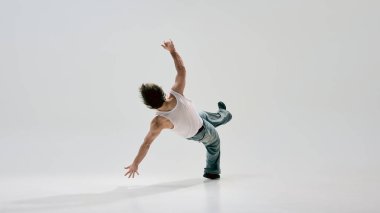 Serbest stil dansçı, sıradan giyinmiş, beyaz arka plana karşı sanatsal akışkanlıkla enerjik bir güç hareketi yaparak yerden kalkıyor. Hareket, kontrol, kendini ifade, akış kavramı.