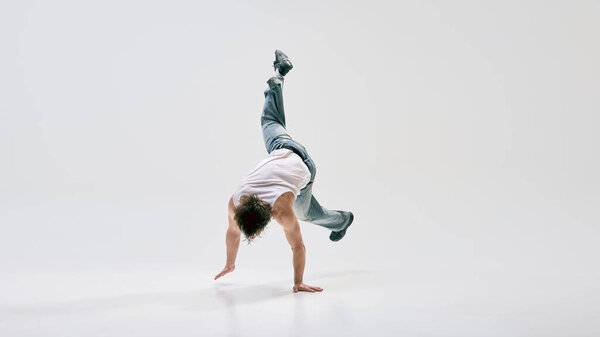 Hip-hop, dancer executing gravity-defying handstand spin with fluid motion against white background. Concept of music and dance, balance, creativity, rhythm, street art, modern culture.