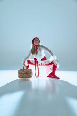 Çömelmiş, elleri sepetin üzerinde duran genç bir kadın, topraklanmış enerjiyi sembolize ediyor, kırılganlığı kontrol ediyor, geleneği gerçeküstücülükle birleştiriyor. Anlamlı moda, sanat, psikolojik zıtlıklar kavramı.