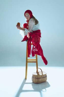 Katmanlı beyaz dantelli ve kırmızı kumaşlı genç kadın tabureye çömelmiş, ekmeği kavrıyor, beyaz arka plana delici bakışlar atıyor. Anlamlı fotoğrafçılık kavramı, duygusal hikaye anlatımı, moda.