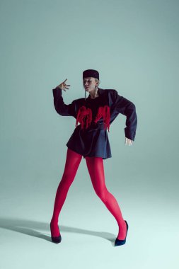 Siyah, büyük beden ceketli, kırmızı taytlı, topuklu ayakkabılı, köşeli duruşlu, el hareketi yapan, kendinden emin bir kadın. Moda anlayışı, gerçeküstü zarafet, yenilikçi performans, drama..