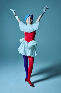 Kırmızı ve mavi tayt, korse ve şehvetli etek giyen neşeli kadın kollarını muzaffer bir şekilde kaldırıyor klasik zarafeti çağdaş oyunculukla birleştiriyor. Moda kavramı, çeşitlilik, kendini ifade etme