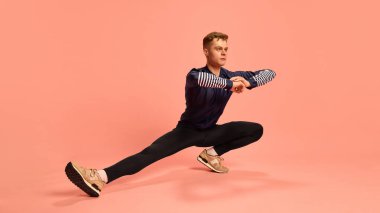 Esnek sporcu kolları çaprazlanmış spor kıyafetleri ve spor ayakkabıları giymiş, pembe arka planda dinamik esneme hareketleri sergiliyor. Spor anlayışı, esneklik, bacak egzersizi.